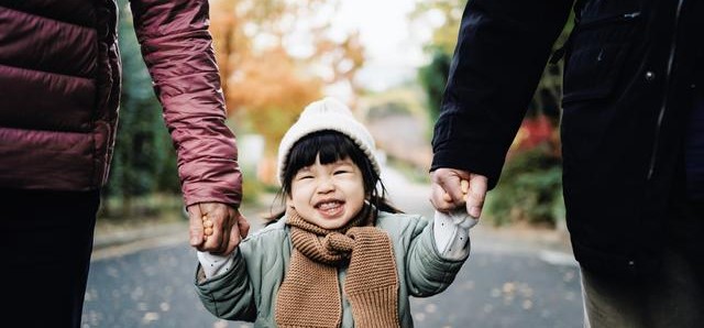A child walking holding hands of two adults