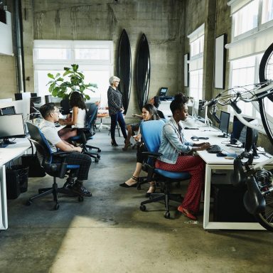 A group of people working in an office space with desks and bicycles they are engaged in conversation